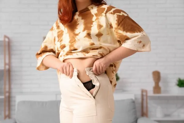 Image of woman trying to do her trousers up after pregnancy weight gain Wilmslow