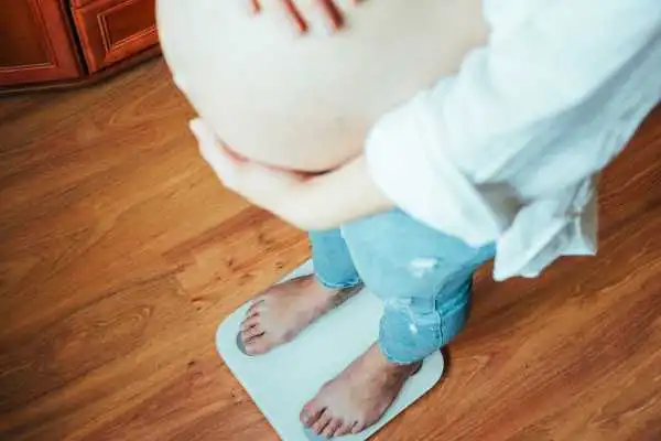 Image of woman weighing herself and experiencing weight gain through pregnancy Wilmslow